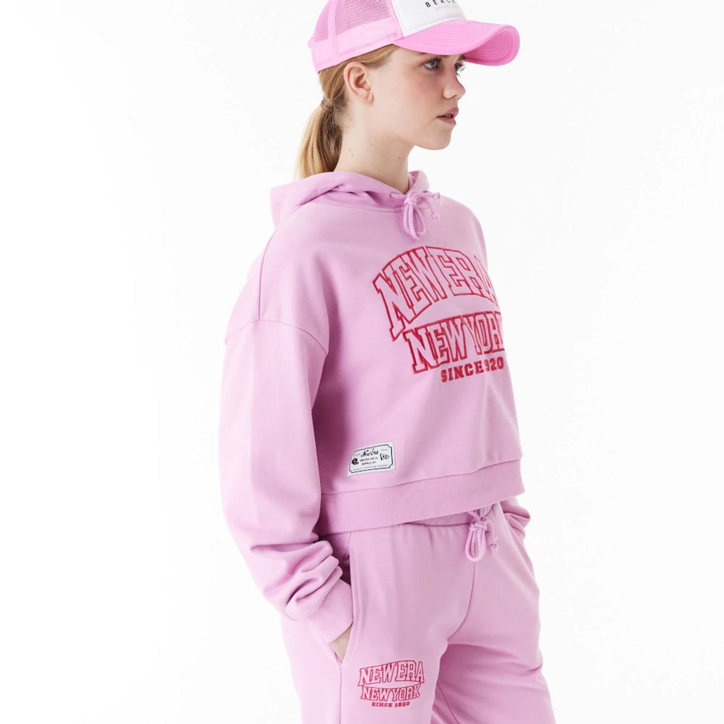 The Female model is wearing New Era Womens Arch Wordmark Pink Crop Pullover Hoodie 3