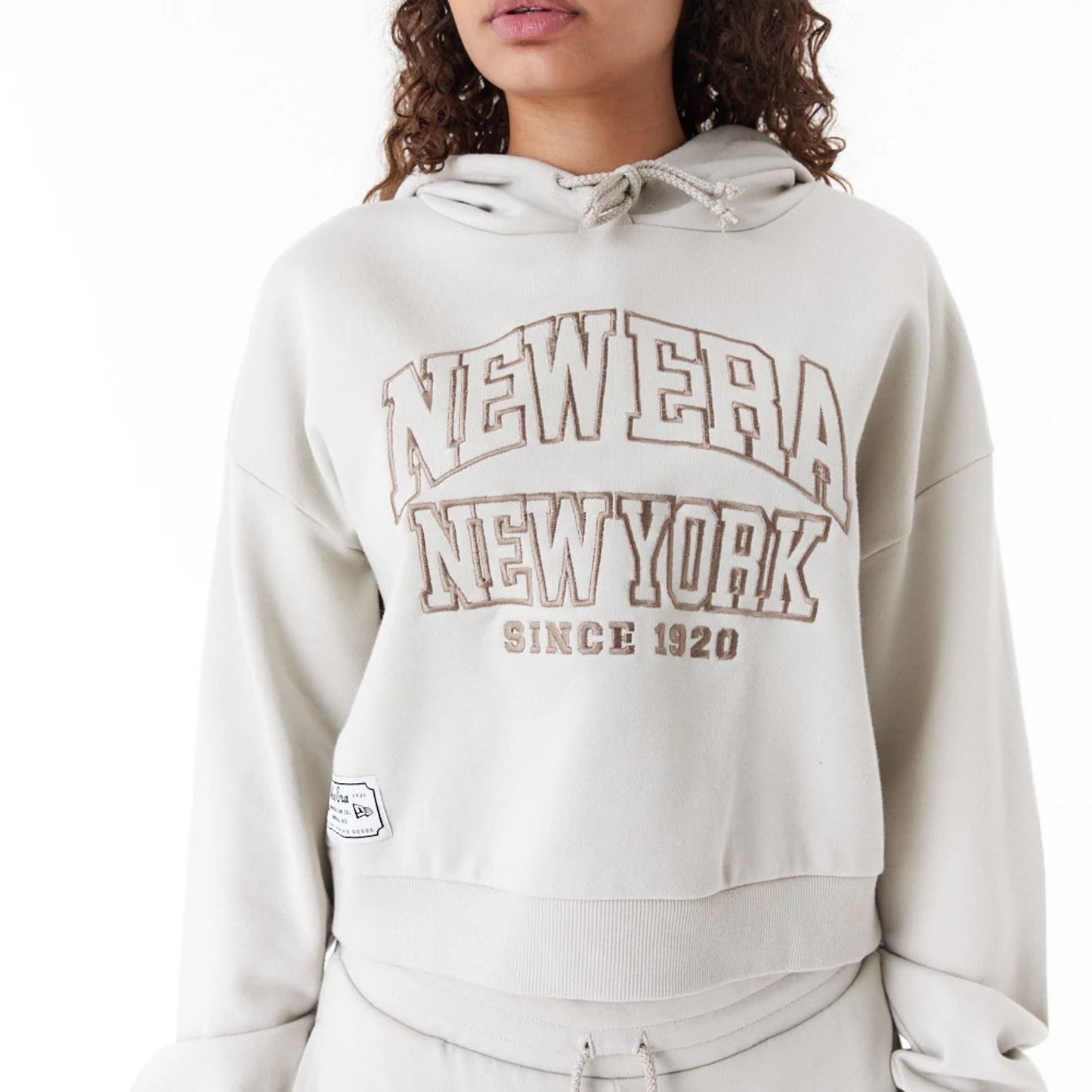 The Female model is wearing New Era Arch Wordmark Stone Womens Crop Pullover Hoodie 4