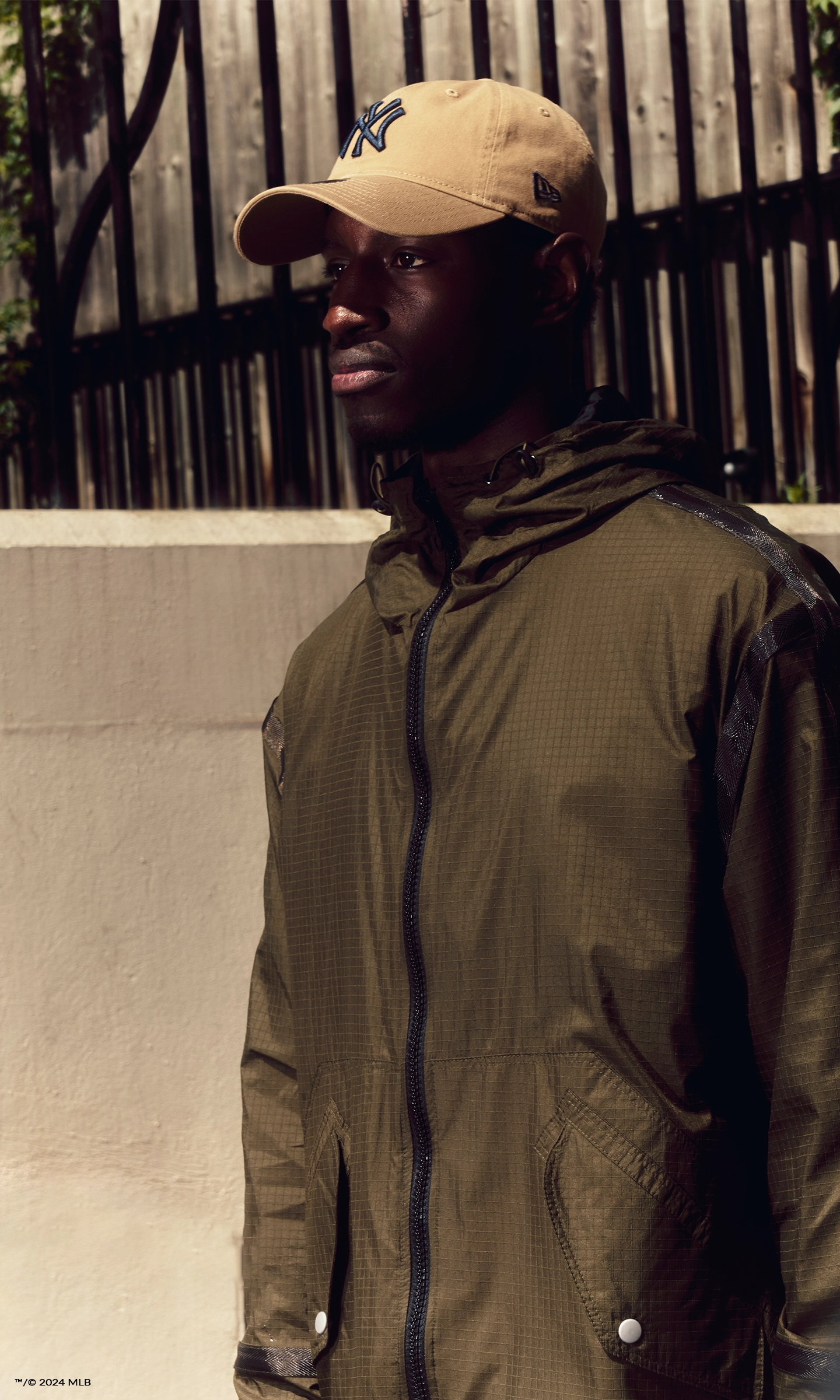 Mobile hero banner of a young man wearing a khaki rain jacket and a beige New York Yankees New Era cap