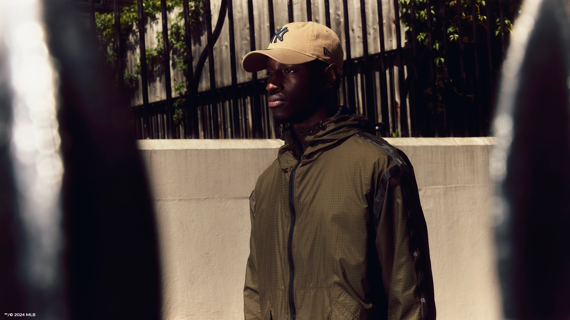 Desktop hero banner of a young man wearing a khaki rain jacket and a beige New York Yankees New Era cap