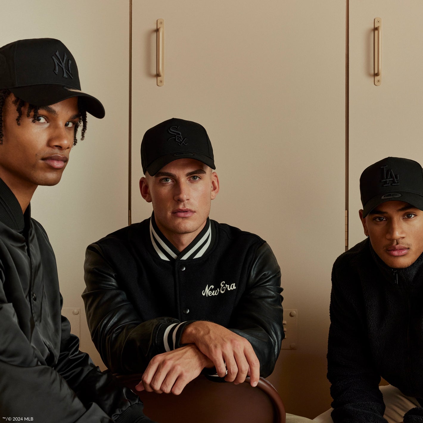 three males wearing black new era caps and bomber jackets 