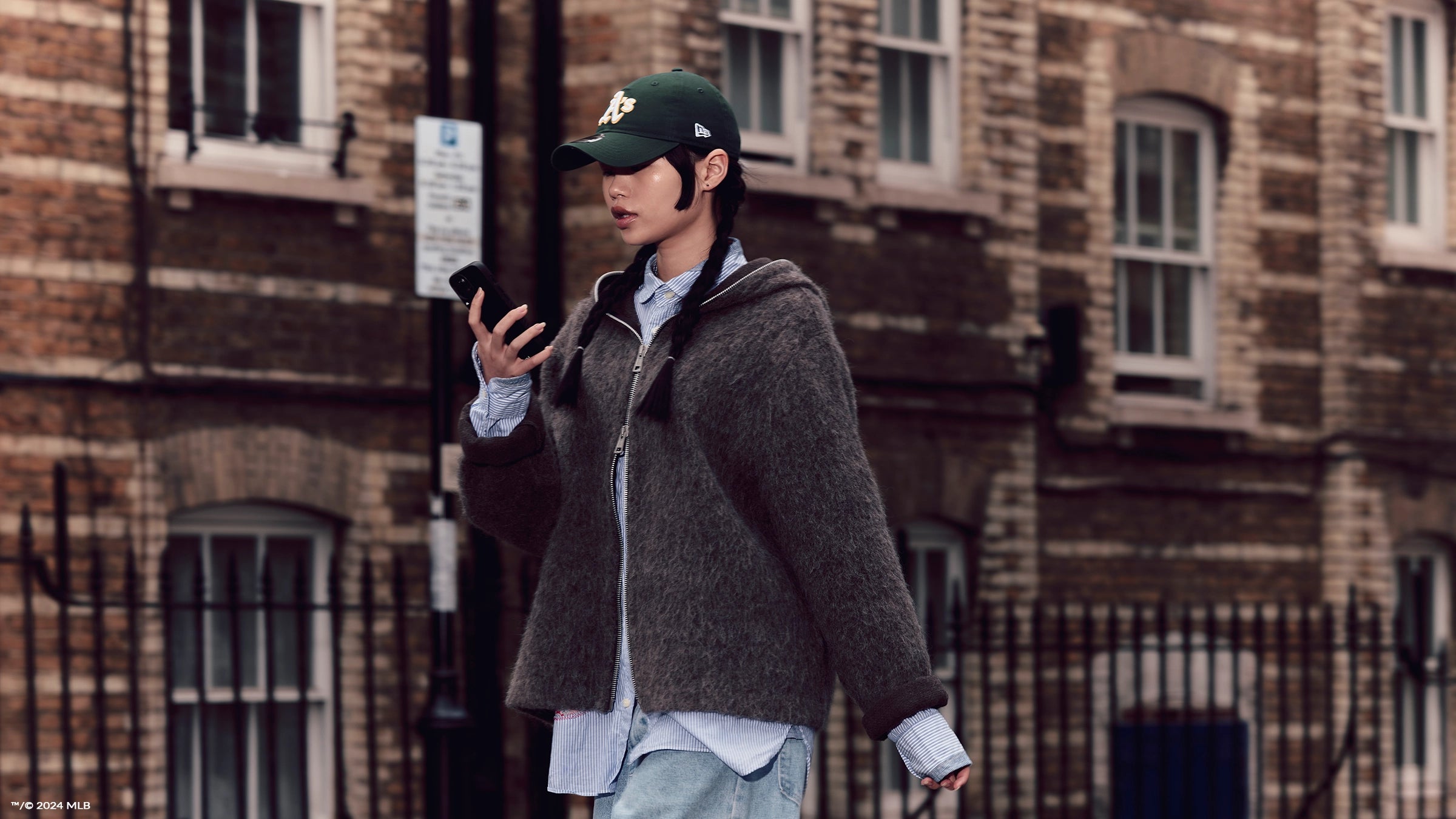 female walking down the street on her phone wearing a green oakland athletics cap landscape