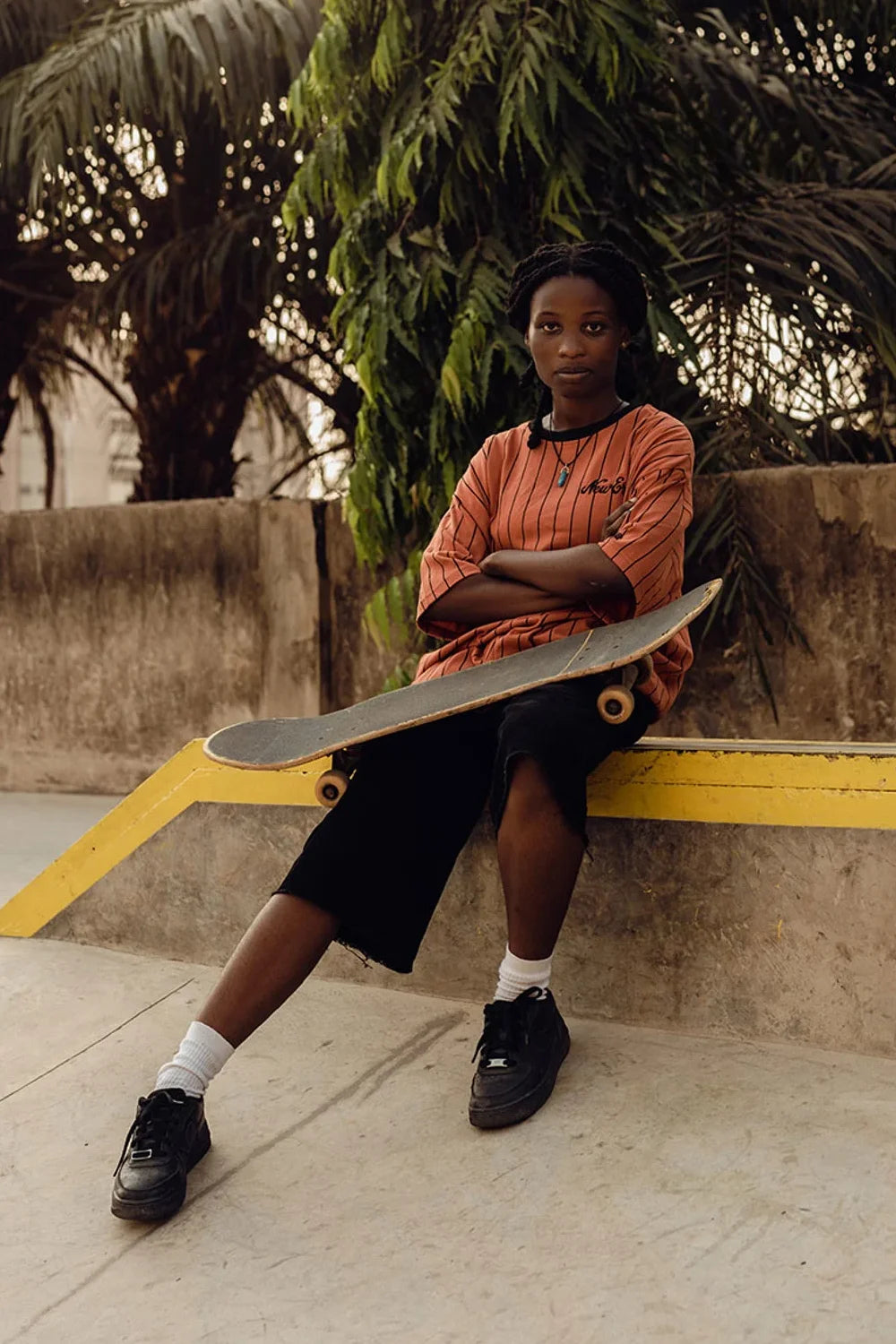 female with a skateboard posing in a new era orange pinstripe t-shirt