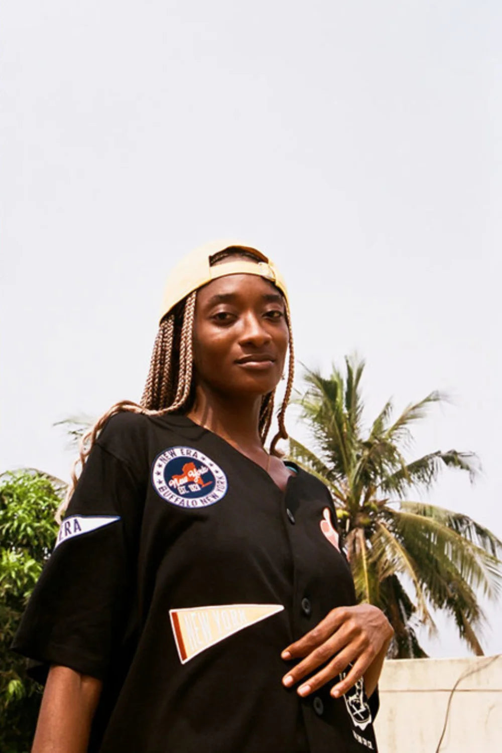 woman wearing a black new era button up jersey and a yellow strapback cap backwards