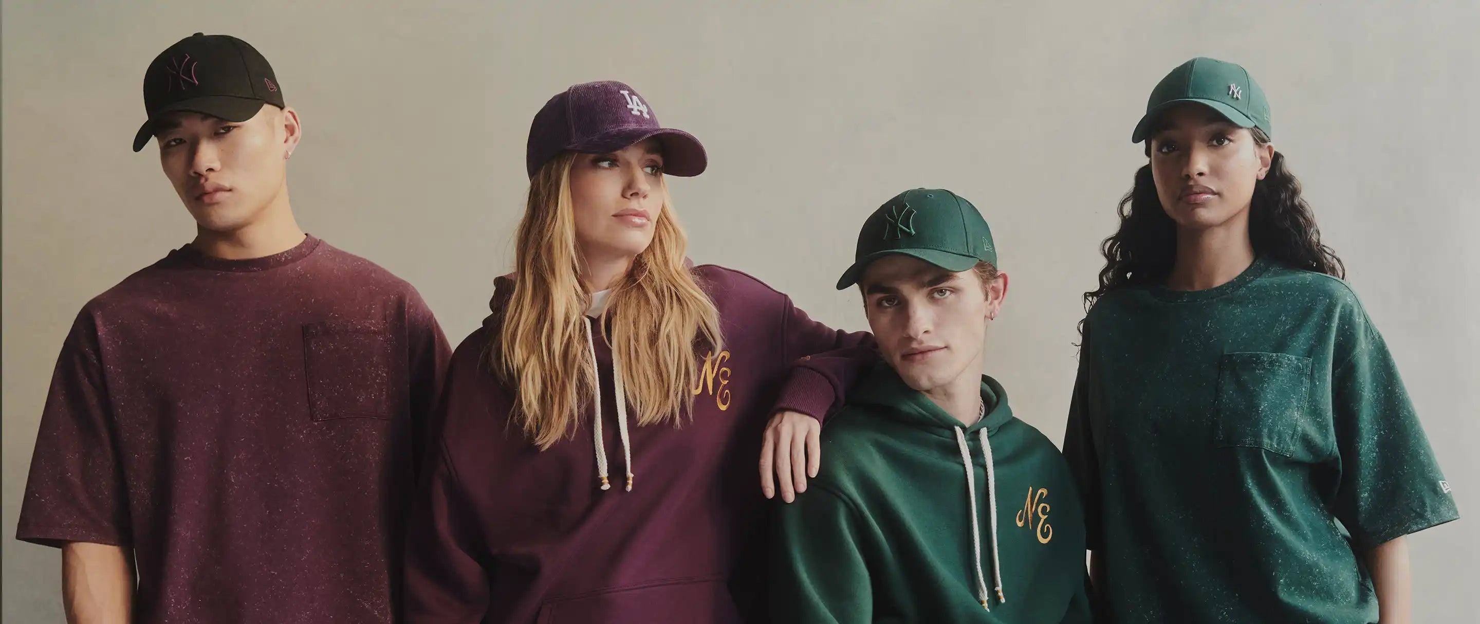 Two men and two women posing next to each other wearing Los Angeles Dodgers and New York Yankees baseball caps. and maroon and green New Era clothing. 