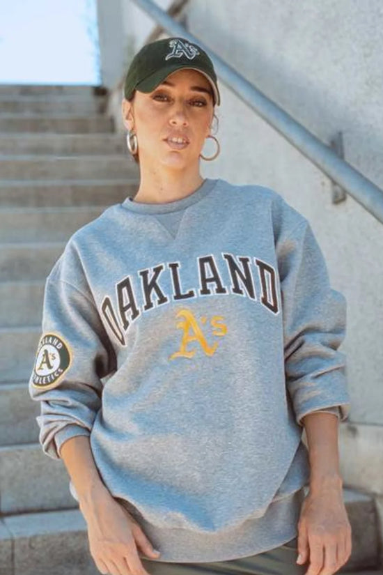 Slide 1:woman wearing a grey oakland athletics sweatshirt and a green oakland athletics cap