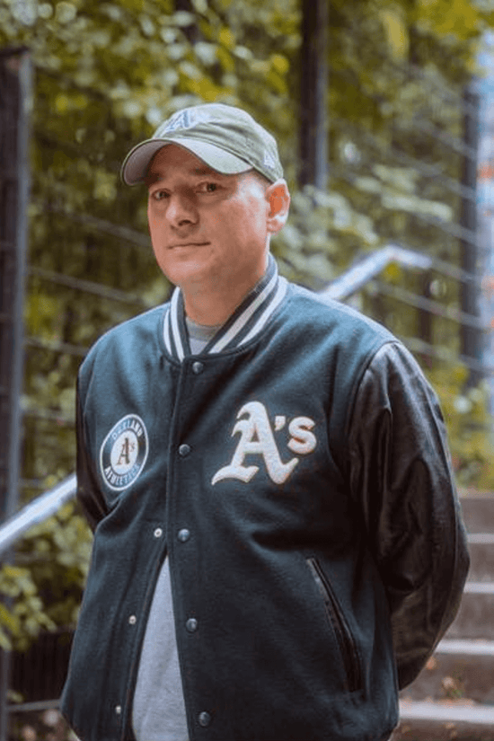 Slide 3:man wearing a black bomber jacket and grey cap with the oakland athletics logo 