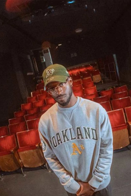 Slide 1:man wearing a grey oakland athletics sweatshirt and khaki cap