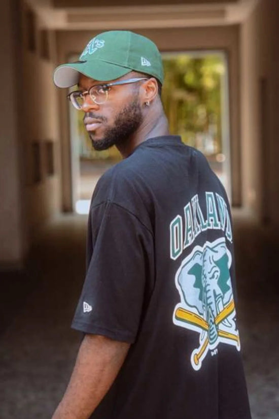 Slide 2:man wearing a black oakland athletics shirt and green cap