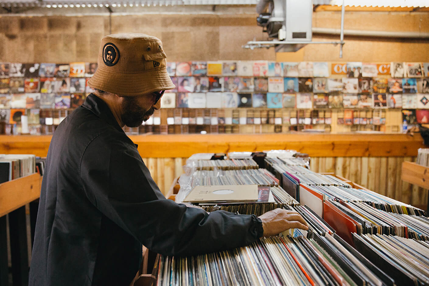 moodymann wearing a new era x moodymann beige bucket hat whilst looking through vinyls