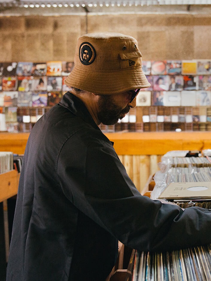 moodymann wearing a new era x moodymann beige bucket hat whilst looking through vinyls portrait 