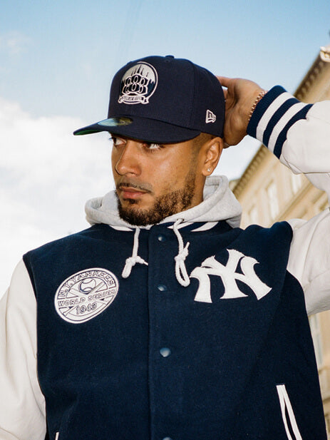 male model wearing a new york yankees blue and white bomber jacket and a blue cap